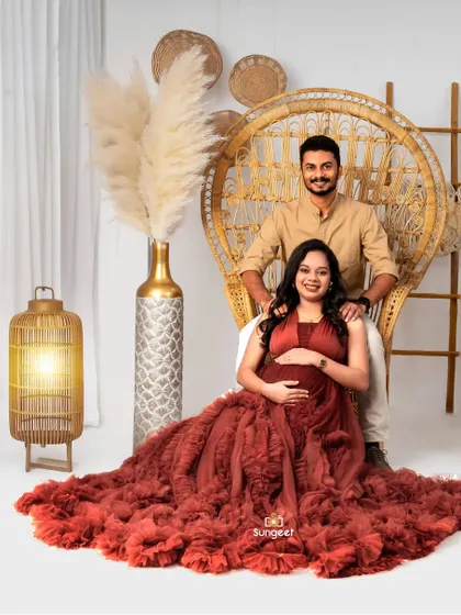 A regal couple's portrait, with the mom-to-be seated in the peacock chair and her partner standing by her side.