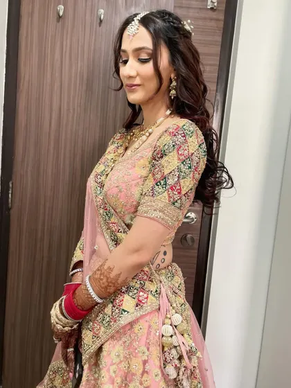 A fresh and natural makeup look for a day wedding function. The focus is on glowing skin and soft curls, adorned with a maang tikka, perfectly complementing her pastel pink lehenga.