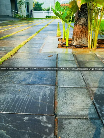 This modern driveway design incorporates strips of grass between large, dark stone tiles, breaking up the hard surface and adding a touch of green.