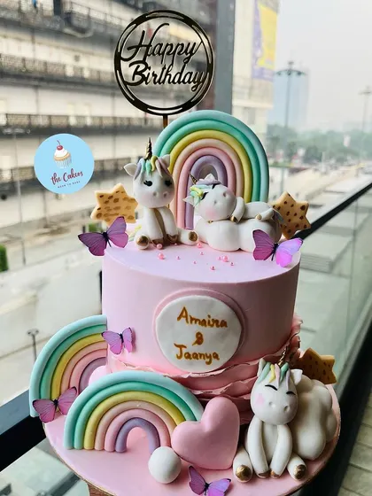 A magical two-tier unicorn cake for a shared birthday. This pink cake is adorned with multiple fondant unicorns, pastel rainbows, stars, and butterflies, making it a dream come true for any unicorn lover.