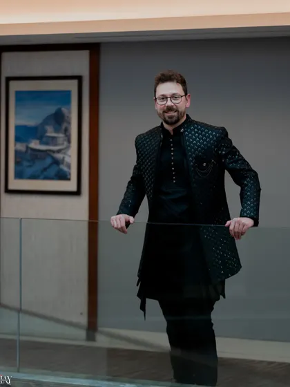 A confident and stylish portrait of the groom. He leans against a glass railing, and the clean lines of the modern interior create a sharp and sophisticated look.