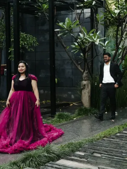A candid moment from a couple's photoshoot in a garden. The client wears our magenta gown with a dramatic ruffled train.