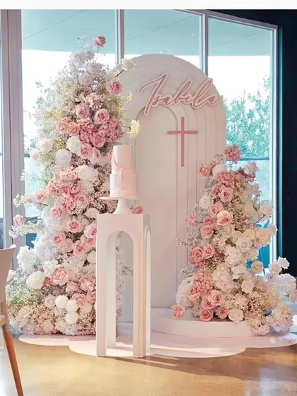 For a baptism, I can create a beautiful and serene setup without balloons. This design features a personalized white arch, a simple cross, and an abundance of soft pink and white flowers for a graceful celebration.