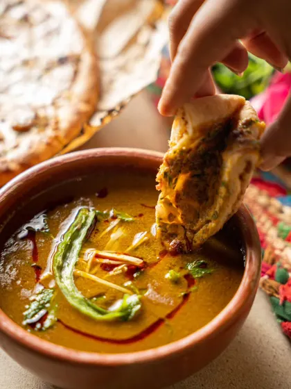A piece of naan being dipped into a rich, savory curry. This simple, relatable action creates a strong craving and connection with the viewer.