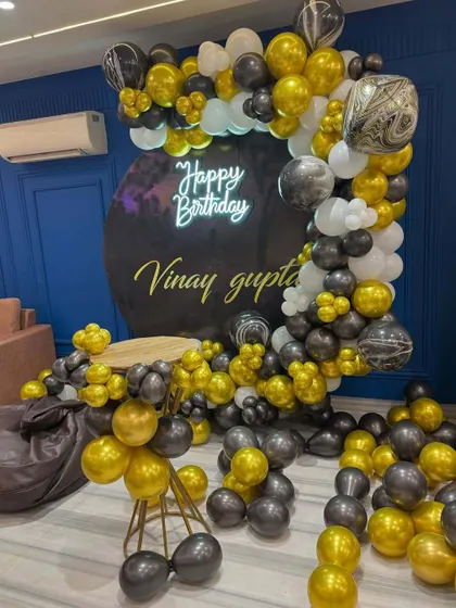 A birthday party with a black, gold, and white balloon arrangement. The decor features a custom black backdrop with the name of the birthday person.