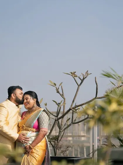 A tender moment between a couple during their baby shower photoshoot, with the husband gently kissing his wife's forehead on a sunny rooftop.