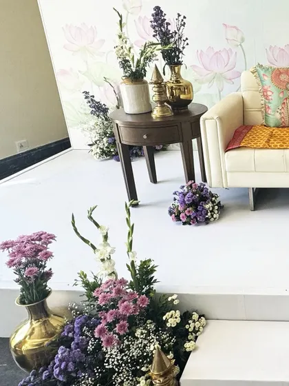 A wide shot of the stage setup, featuring a lotus-print backdrop, a clean white stage, and lush floral arrangements in shades of purple and white, creating a divine and peaceful setting.