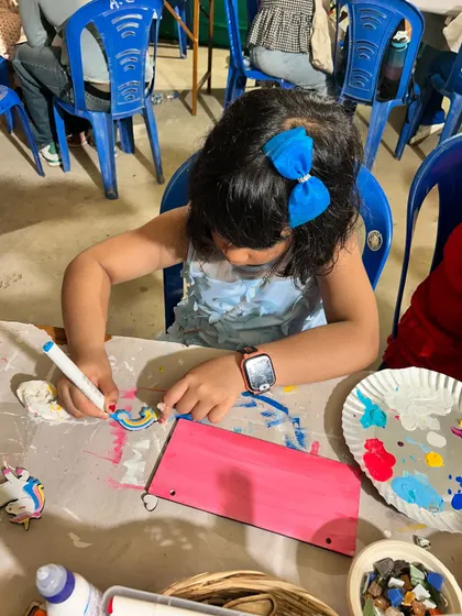 A young artist deeply focused on painting a rainbow on her project at our pop-up stall.