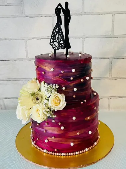 A two-tier cake celebrating the color of the year, Viva Magenta. The textured buttercream is accented with pearl details and fresh white flowers, creating a vibrant and stylish look for an anniversary or engagement.