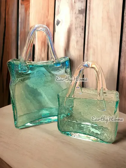 The glass handbag vase shown against a rustic wooden background. Its iridescent finish and unique shape make it a stunning decorative item.