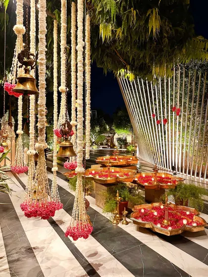 The entrance walkway lined with hanging floral strings, temple bells, and urli water features.