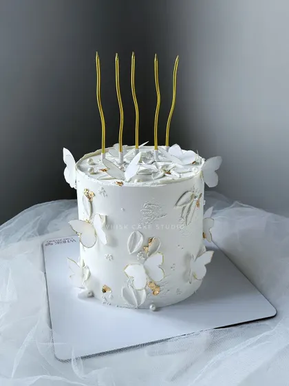 Elegance in white. A simple white cake adorned with edible butterflies and gold leaf for a touch of sophistication.