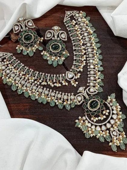 A layered necklace set with a long Rani Haar and a matching choker. This design is perfect for brides, featuring rich green or red stones and intricate detailing for a complete and opulent look.