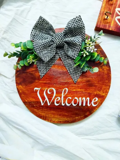 The "Welcome" sign, a simple yet beautiful way to greet guests. The combination of the dark wood stain, white script, and decorative bow gives it a classic, rustic charm.