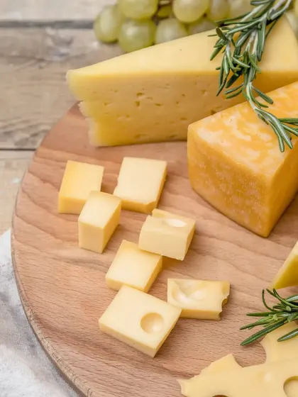 A rustic wooden board with wedges of Swiss and cheddar cheese, garnished with fresh rosemary. This simple yet elegant presentation highlights the quality of the ingredients.
