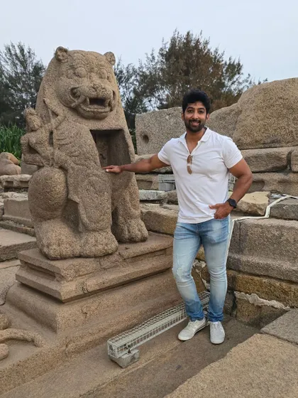 Posing with a carved lion statue, a common motif in Pallava architecture, representing royalty and power.