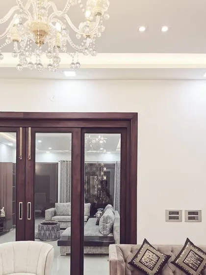 A detail shot of the living room in Villa 9/21B, showing the elegant crystal chandelier and recessed ceiling lighting. This view through the dark wood-framed doors highlights the depth and interconnectedness of the spaces we design.