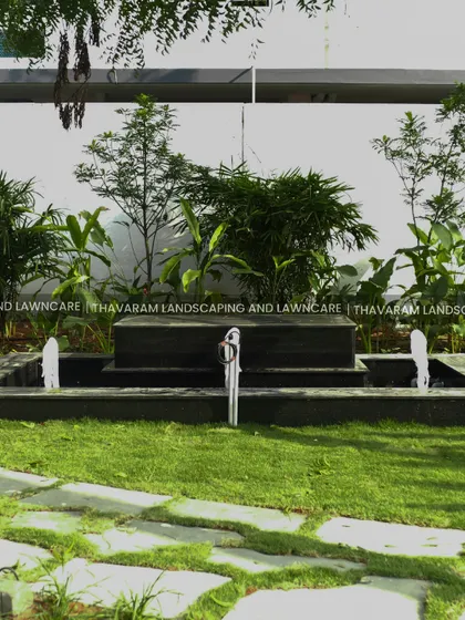 A frontal view of the black stone, multi-tiered water fountain, surrounded by a lush lawn and tropical foliage.