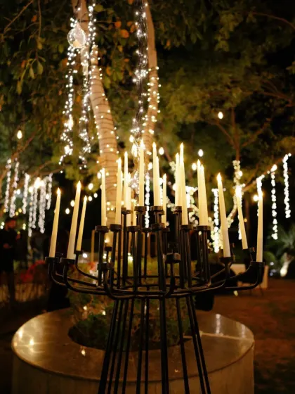 A modern candelabra stands as a sculptural element amidst trees wrapped in lights. We mix different styles of lighting fixtures to create a layered and interesting ambiance.
