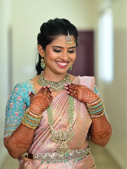 The bride looking joyful, her custom embroidered blouse perfectly complementing her pastel pink silk saree.