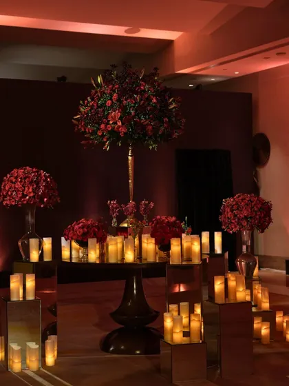 An elegant entrance display with red florals and candles set on mirrored pedestals, welcoming guests to the 'Raga Saga' reception.