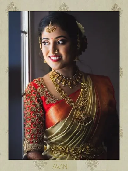 A bride wearing a vibrant red blouse with heavy gold embroidery on the sleeves. The design is a classic choice for a traditional South Indian muhurtham ceremony.