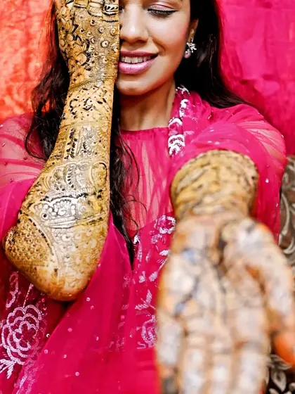A playful pose from a happy bride, peeking through her mehandi-covered arm.