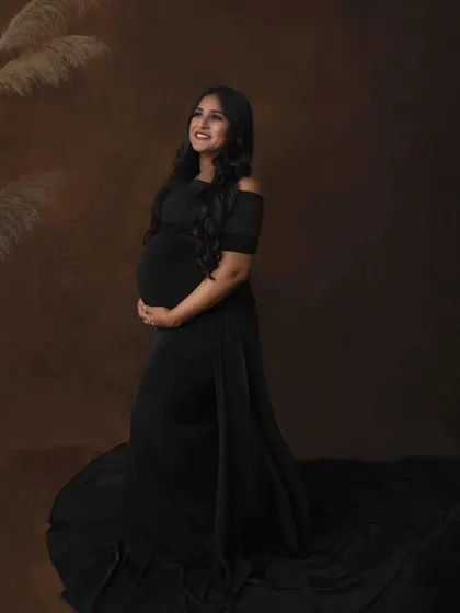 A hopeful and radiant portrait, with the mother-to-be looking up with a bright smile. The flowing black gown and simple styling create a look that is both elegant and timeless.