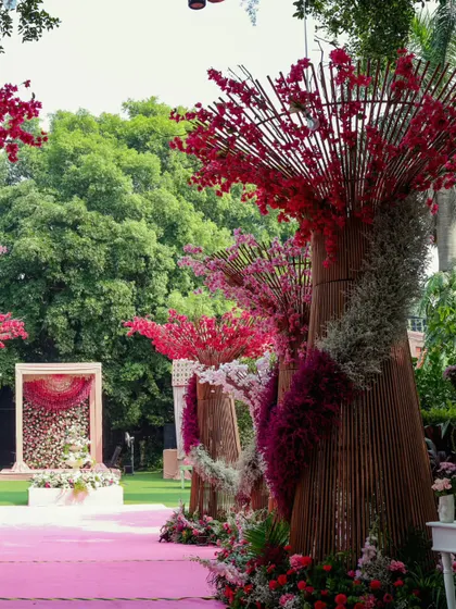 A view down the pink carpet aisle, flanked by sculptural floral trees, leading to a beautiful mandap or stage in the distance.