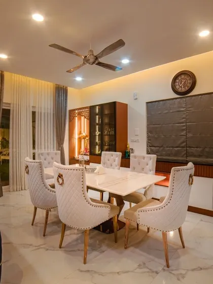 The elegant dining space in Ms. Megha Joshi's home, featuring plush, quilted chairs and a marble-topped table. The adjacent pooja unit and crockery cabinet are seamlessly integrated, showcasing our expertise in functional and beautiful design.