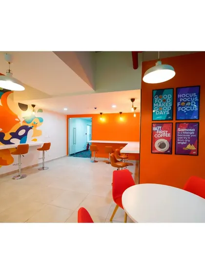 The Mindsprint canteen combines high-top bar seating with traditional tables. The orange accent wall with fun, food-related posters adds a playful touch to the dining experience.