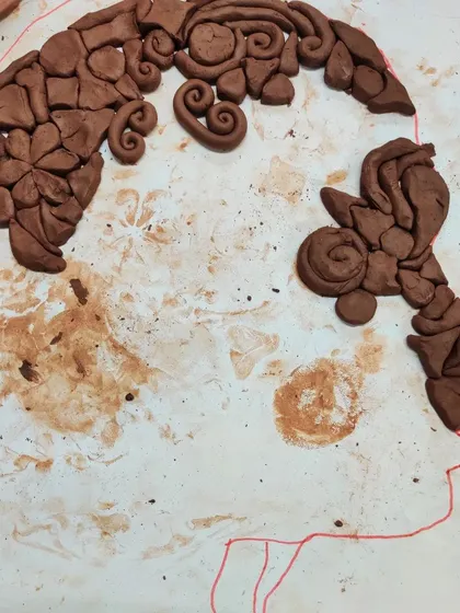 A work in progress, this clay silhouette shows a child using different shapes and swirls to create hair. This is a wonderful exercise in design and composition for young artists.