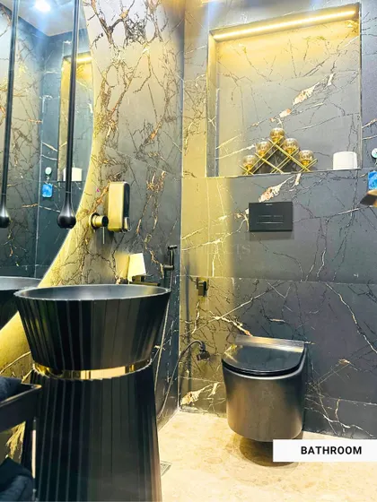A bold and dramatic bathroom in Amar Colony, completely clad in black marble with gold veins. The pedestal sink and teardrop pendant lights create a powerful statement of luxury.