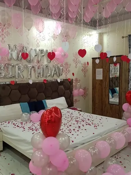 A sweet pink and white birthday room surprise with ceiling balloons, foil letters, and rose petals scattered on the bed.