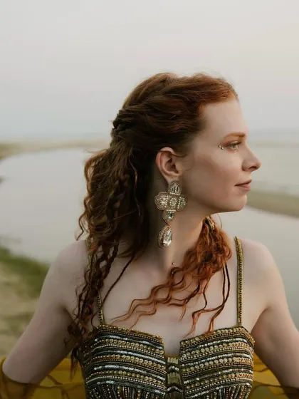 A profile of the bride at the sundowner, highlighting her soft, romantic hairstyle and statement earrings that perfectly accessorized her bohemian beach look.