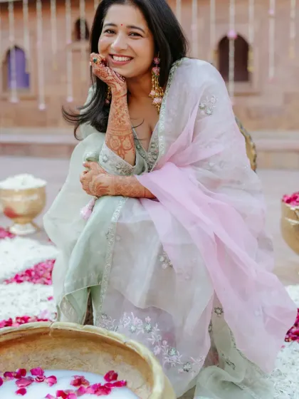 The beautiful bride seated by a traditional brass bowl filled with milk and rose petals for her Chooda ceremony.