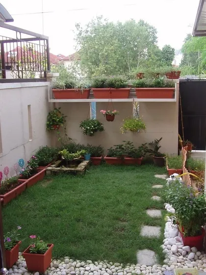 A small backyard design that maximizes green space. It features a central lawn, a stone stepping path, and a border of white pebbles, with planters arranged at different levels.