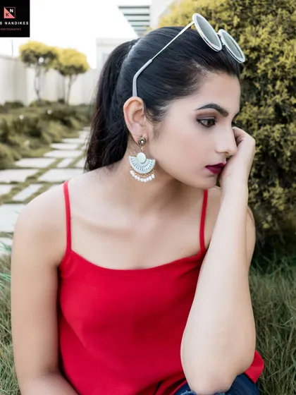 A thoughtful outdoor portrait. The model sits in the grass, her gaze directed away from the camera, creating a candid and contemplative mood with beautiful natural light.