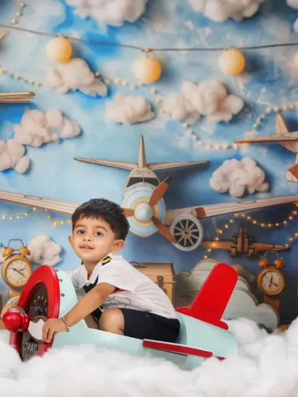 A full view of our pilot theme, where a happy toddler sits in a toy plane, surrounded by clouds, clocks, and directional signs.