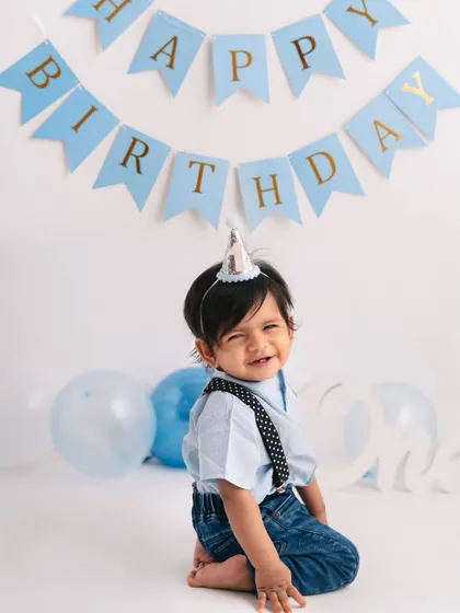 A cheeky little smile from the birthday boy. Dressed in a party hat and cute suspenders, he's ready for his first birthday celebration.