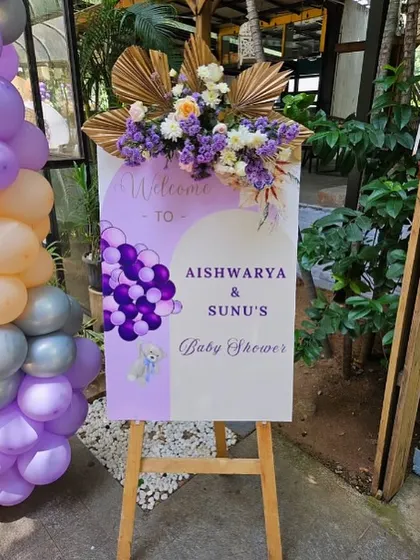 A personalized welcome sign for Aishwarya & Sunu's baby shower, topped with a lavish floral arrangement.