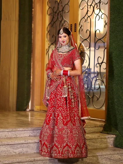 A full-length bridal portrait, showcasing the bride's magnificent red lehenga as she stands elegantly on a step.