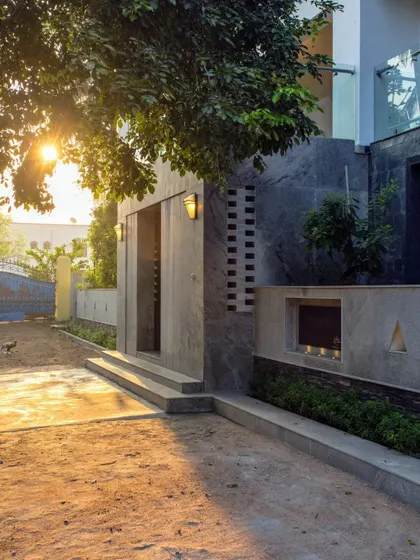 The entrance at sunset, with integrated lighting highlighting the different textures of the facade, from the smooth concrete to the rough stone and perforated brickwork.
