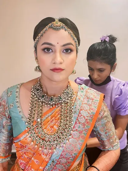 A candid shot during the getting-ready process. The bride is looking serene as her team helps with the final touches on her jewelry.