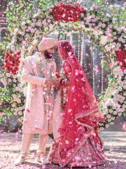 A magical moment as a Sikh couple shares their first look under a stunning floral arch, with a cascade of pink petals showering down around them. This image perfectly captures the joy and emotion of the Varmala ceremony.