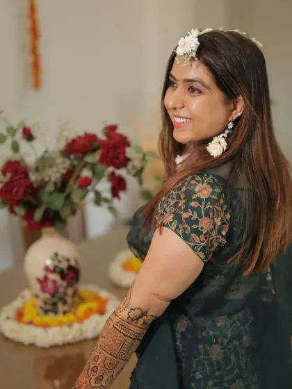 A candid shot of the bride during her mehandi ceremony. The intricate design on her arm is visible, complementing her floral jewelry and outfit.