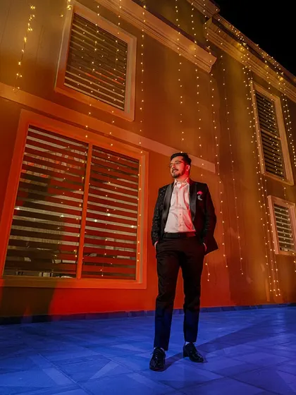 The groom stands against a beautifully lit building at night, a cool and stylish portrait that makes him look like the star of his own movie.