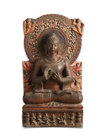 This magnificent stone stele of Gautam Buddha from 8th century North India is a testament to the rich history of ancient Indian sculpture. The Buddha is depicted seated in 'dhyanasana' with his hands in the 'dharmachakra' mudra, conveying a serene expression. The intricate details, from the scrolling nimbus to the worshippers on the throne, highlight its historical and artistic importance.