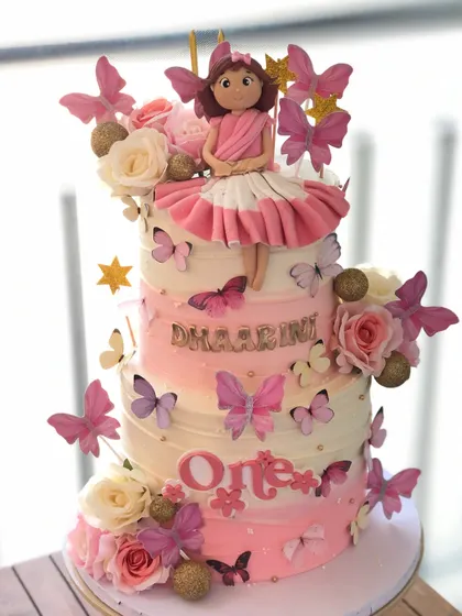 A grand two-tiered butterfly cake with a custom doll topper, perfect for a first birthday celebration.