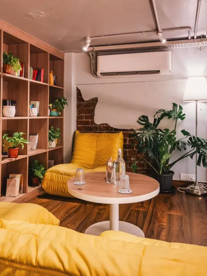 This cozy nook at Stand By Coffee with its bright yellow seating and bookshelf shows a comfortable corner for guests. This lifestyle interior shot helps customers imagine themselves relaxing with a coffee and a book.